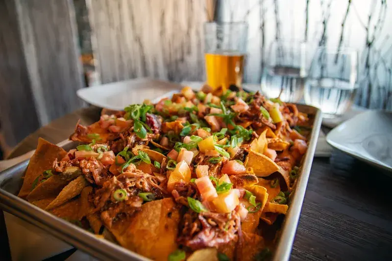 A sheet-pan of loaded pulled-pork nachos with tomato, jalapeño and spring onion served with a cold beer at Alaska Rendezvous Lodge